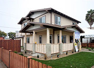 Exterior of a Habitat for Humanity house under construction in Los Angeles, two stories with a wrap-around front porch and fenced in yard.